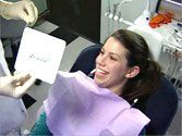 A woman in a dental chair smiles after being treated with Zoom teeth whitening.